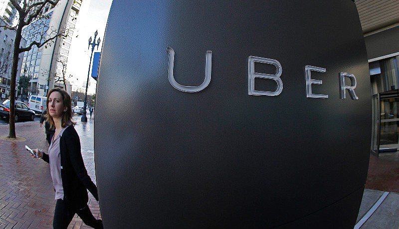 In this file photo taken Tuesday, Dec. 16, 2014, a woman walks past the company logo of the internet car service, Uber, in San Francisco.