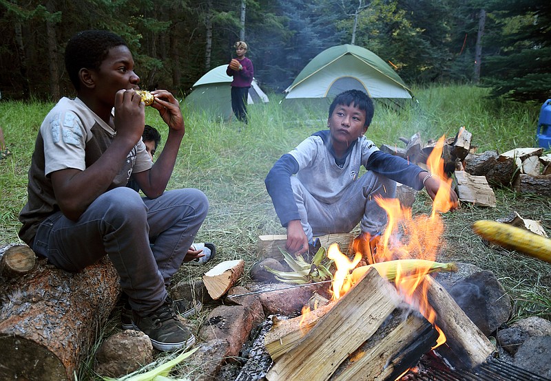 In this Sept. 10, 2016, photo, Justin Mbelechi, 13, and Bidesh Magar, 14, roast corn at their campsite in Evergreen, Colo. The two belong to a Colorado Boy Scout troop that is made up almost entirely of refugees. At campouts, traditional American food like hot dogs and trail burgers is replaced by fish head stew, fire-roasted corn and Chatpate, a popular Nepalese street snack.