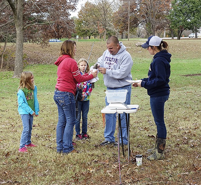 Courtney Cofelt holds a rainbow trout caught by her granddaughter, Dayton, 7, while Clay Caswell of the Fulton Parks and Rec department notes its size. The trout stocked for this fishing tournament in November are still waiting to be caught in the pond at Veterans Park.