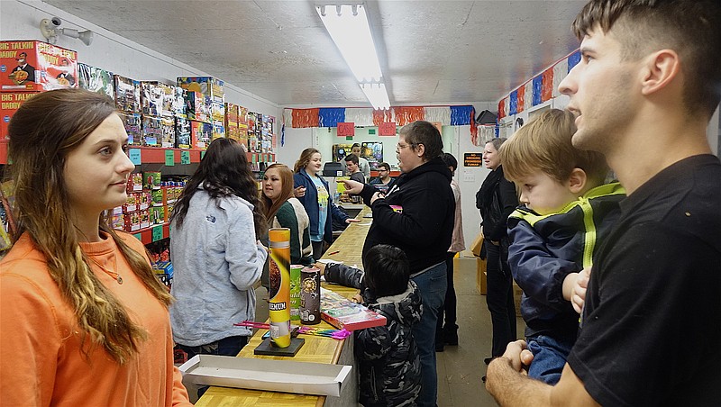 Dakota Cummings is ready to celebrate the new year with his son Raylan by purchasing fireworks from the Cornerstone Assembly of God store. Church member Tristen Lee is helping. In the background are Shauna Lee, Nina Vuniga, Hollie Rhine, Carter Gonzales and youth pastor Joseph Parker.