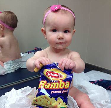 In this photo provided by the Carrie Stevenson, her daughter Estelle holds a bag of peanut snacks in her pediatrician's office at age nine-months, in Columbus, Ohio. Most babies should start eating peanut-containing foods well before their first birthday, say guidelines released Thursday that aim to protect high-risk tots and other youngsters, too, from developing the dangerous food allergy. The new guidelines from the National Institutes of Health mark a shift in dietary advice, based on landmark research that found early exposure dramatically lowers a baby's chances of becoming allergic. 
