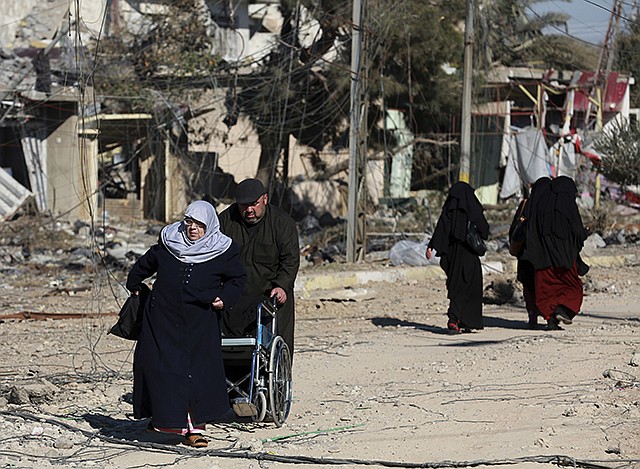 A man pushes a woman in a wheelchair Thursday in their neighborhood that was recently liberated from Islamic State militants as life begins to return to the eastern side of Mosul, Iraq. Small stalls and carts have sprung up outside the bombed-out restaurants and cafes in eastern Mosul, selling fresh vegetables, cigarettes and cellphones to the thousands of civilians still living in neighborhoods where the Iraqi military has driven out the extremists of the Islamic State group.