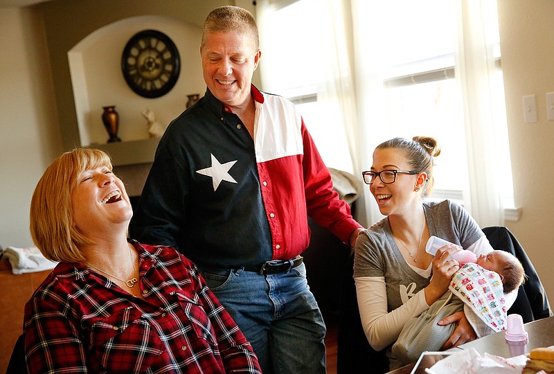 In this Jan. 10, 2016, photo, Tracey Thompson, left, the 54-year-old Collin County woman who gave birth to her granddaughter Kelcey McKissack, right, as a surrogate mother, laughs while telling stories of the birth with her husband Ben Thompson, center, and daughter Kelley McKissack at McKissack's home in Wylie, Texas. 