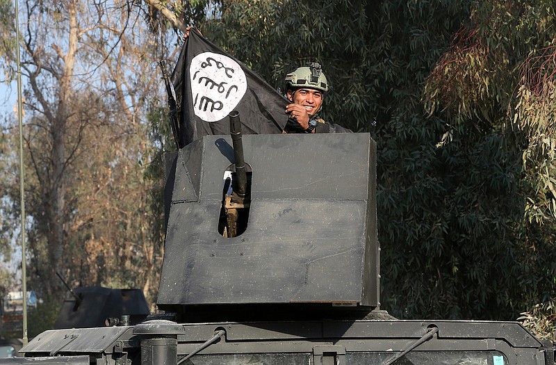 A soldier with elite counterterrorism forces rides atop of an armoured vehicle celebrating as he holds a flag of the Islamic State group as Iraqi special forces fight against Islamic State militants to regain control of Mosul University, in the eastern side of Mosul, Iraq, Saturday, Jan. 14, 2017.