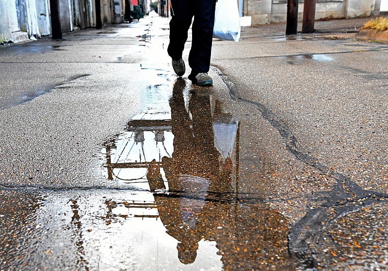 William Jones walks through an alley as seen reflected through a puddle Monday in downtown Texarkana. Heavy rains swept through the Texarkana area Monday morning and afternoon. 
