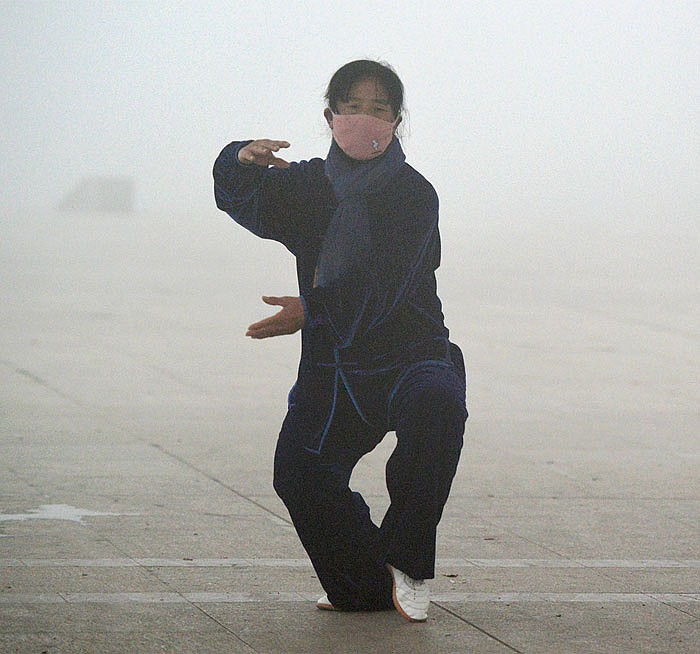 A woman wearing a protective mask practices tai-chi in  park blanketed by dangerous smog in China.