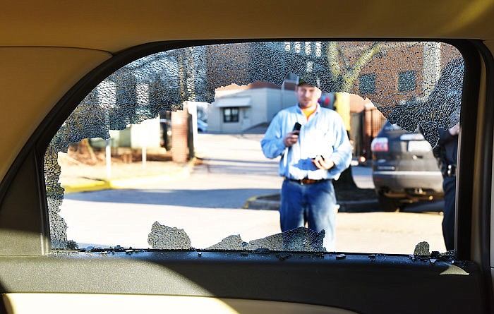 Keith Arnel with Facilities Management can be seen through the shattered rear window of a car. He holds a handful of ceramic pieces while contacting a co-worker to clean up the broken vehicle glass on the state parking lot. An insulator on an Ameren Electric power line located just below St. Peter School exploded Wednesday afternoon, sounding like a small explosion and sending pieces of ceramic insulator flying more than 150 feet through the air. One chunk hit this vehicle window, shattering it. 