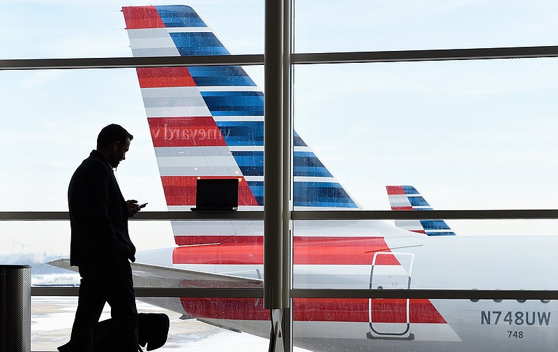 In this Jan. 25, 2016, file photo, a passenger talks on the phone as American Airlines jets sit parked at their gates at Washington's Ronald Reagan National Airport.