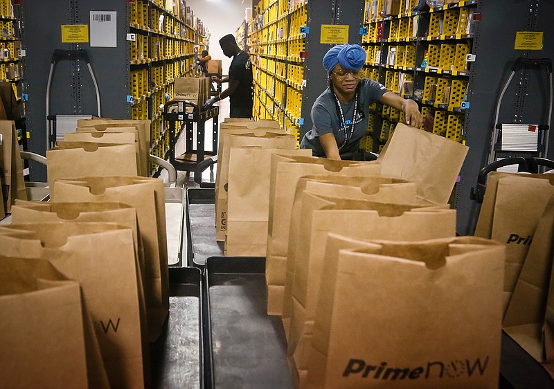 In this Wednesday, Dec. 21, 2016, file photo, Miracle Stewart, right, an employee of Amazon PrimeNow, prepares bags to fill with orders from customers making purchases, at a distribution hub in New York. From Wal-Mart to General Motors to Amazon, a growing number of the world's largest companies appear to be trying to get in step with President-elect Donald Trump's demand that employers hire and keep jobs at home. 