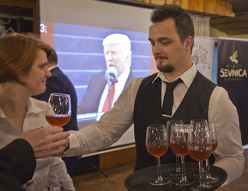 A waiter delivers drinks to guests Friday as they watch a televised broadcast of the inauguration of Donald Trump at a restaurant in Sevnica, Slovenia.