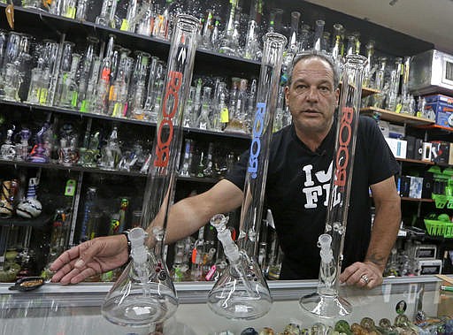 Jay Work talks to a reporter as he places tobacco on the counter next to three authentic Roor water pipes, at his Grateful J's smoke shop Thursday, Jan. 12, 2017, in Margate, Fla. High-end German glass water pipe maker Roor and its American licensee are filing lawsuits against smoke shops and mom-and-pop convenience stores in Florida, California and New York alleging that they are selling Roor counterfeits, violating its trademark. 