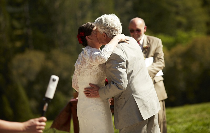 In this March 2014 photo provided by Eva Zimmerman, Zimmerman, left, kisses her father Michael Zimmerman, as her stepfather Jack Shoemaker, the officiant of the ceremony, looks on in the background during the ceremony in Berkeley, Calif. 