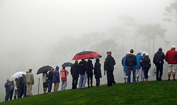Spectators stand in the fog Friday along the ninth green of the Spyglass Hill Golf Course in Pebble Beach, Calif.