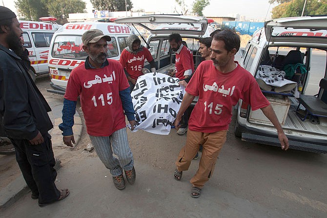 Pakistani volunteers carry the dead body of an alleged militant killed in a crackdown operation by security forces to a mortuary Friday in Karachi, Pakistan. Pakistani security forces arrested dozens of suspects in sweeping raids a day after a massive bombing claimed by the Islamic State group killed dozens at a famed Sufi shrine in a southern province.