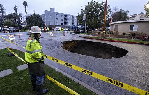 A worker keeps watch on a sinkhole Saturday, Feb. 18, 2017, in Studio City, north of Los Angeles. Two vehicles fell into the 20-foot sinkhole on Friday night and firefighters had to rescue one woman who escaped her car but was found standing on her overturned vehicle.