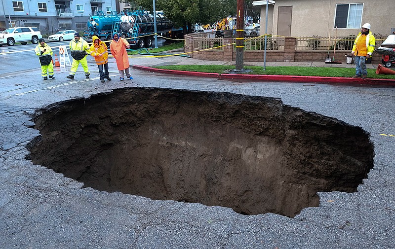 Inspectors examine a sinkhole Saturday, Feb. 18, 2017, in Studio City, north of Los Angeles. Two vehicles fell into the 20-foot sinkhole on Friday night and firefighters had to rescue one woman who escaped her car but was found standing on her overturned vehicle.