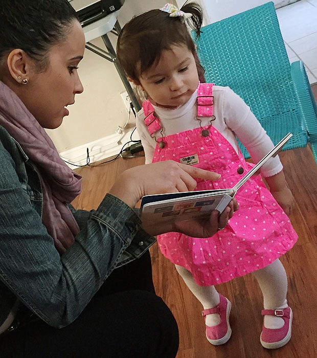 Caseworker Stephanie Taveras, left, reads a book with 20-month-old Gracey Niebla, right, at the child's home in Providence, Rhode Island. The city is in the third year of its effort to boost language skills for children from low-income families by equipping them with audio recorders that count every word they hear. During home visits, social workers go over the word counts with parents and suggest tips to boost children's language skills.