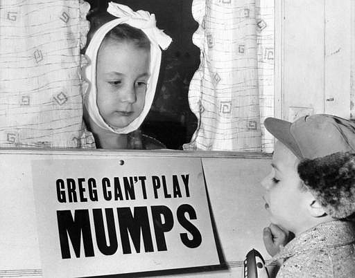 In this Jan. 16, 1957 file photo, Jon Douglas, 6, right, visits his friend, Greg Cox, standing behind a sign warning he has mumps, on the door of his home in Altamont, Ill. Fifty years ago, mumps was once a childhood rite of passage of puffy cheeks and swollen jaws. That all changed with the arrival of a vaccine in the late 1960s, and mumps nearly disappeared. But in 2017, the U.S. is in the midst of one of the largest surges in decades. 