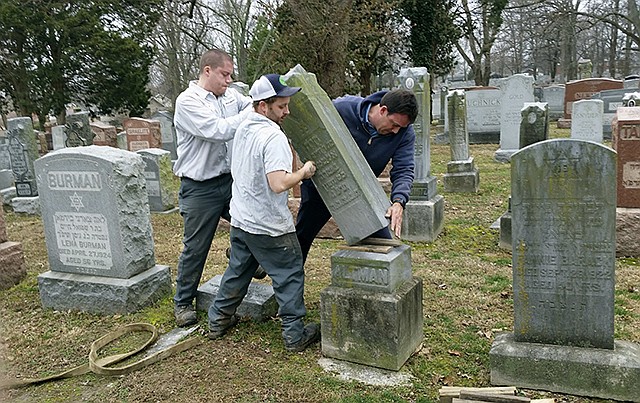 Rosenbloom Monument Co. workers from left, Nathan Fohne, Derek Doolin and Philip Weiss hoist a headstone at the Chesed Shel Emeth Cemetery in University City, where more than 150 headstones were tipped over. No arrests have been made. The cemetery is getting a show of support from cleanup volunteers, well-wishers and financial contributors from across many faiths.