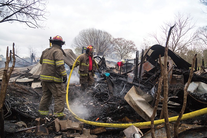 Members of the Redwater Volunteer Fire Department spray hot ash Monday and look for family photographs at a home that burned Sunday. 