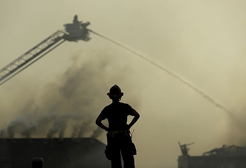 A firefighter watches from the scene of an apartment complex fire as firefighters douse fires at nearby homes Monday, March 20, 2017, in Overland Park, Kan. Once one roof caught fire, embers jumped from roof to roof, spreading the blaze, said Overland Park Fire Department spokesman Jason Rhodes.