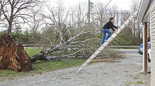 Paula Timms of Caraway climbs up to the roof of her mother-in-law's house to help with repairs Saturday after Friday night's storm in Jonesboro, Ark., March 25, 2017. An uprooted tree took also knocked out the power to the house. Storms demolished mobile homes in Arkansas and a church in Louisiana as a menacing weather system threatened several states across the South and Midwest, authorities said. (Staci Vandagriff /The Jonesboro Sun via AP)