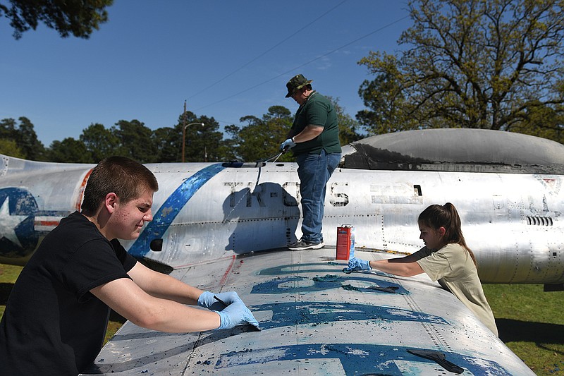Texarkana Arkansas Civil Air Patrol 95th Composite Squadron members, Alexander Hoffmeister, left, Emma LaFors, right, and Jonathan McIntyre work to remove faded paint and decals from the T-33 training plane on display Sunday at Spring Lake Park in Texarkana, Texas. The group received new official decals from the Wright-Patterson Air Force Base in Dayton, Ohio, which owns the plane. Local Civil Air Patrol Commander Lt. Col. Loren Ainsworth plans to have the plane shined, with fresh decals and paint over the coming months.