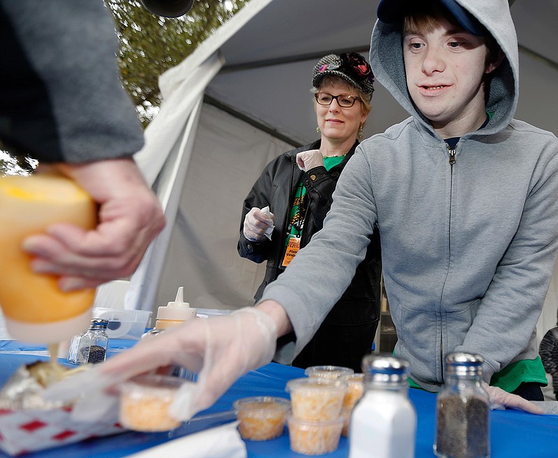 In a March 4, 2017 photo, Erika Burkhardt, left, looks on as Scots Cafe student Chris Wheeler serves Karl Neumann, far left, during the North Texas Irish Festival at Fair Park in Dallas. The cafe is part of the Highland Park Independent School District's transition program, in which young adults with special needs learn work skills by handling and preparing food for school and local catering events. 