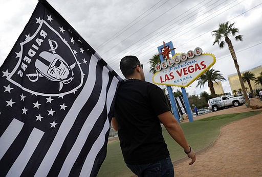 Matt Gutierrez carries a raiders flag by a sign welcoming visitors to Las Vegas, Monday, March 27, 2017, in Las Vegas. NFL team owners approved the move of the Raiders to Las Vegas in a vote at an NFL football annual meeting in Phoenix.