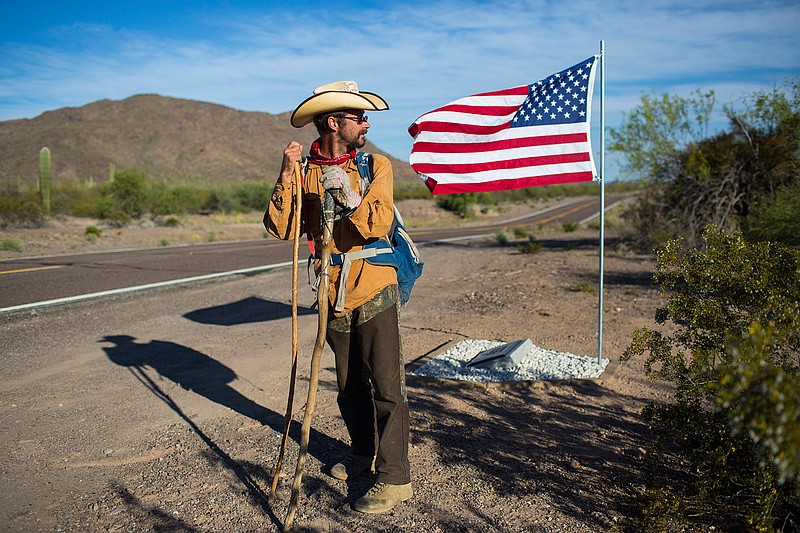 In this Monday, April 3, 2017 photo, Mark Hainds of Andalusia, Alabama, stands next to a road memorial honoring a Border Patrol agent killed in a car accident near Why, Arizona. Hainds is attempting to walk the length of the U.S.-Mexico border on foot. 