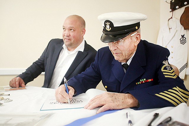 Retired U.S. Coast Guard Master Chief Rodger Dewey signs a copy of his book Wednesday at Heisinger Bluffs' retirement community. Matt Grayson, left, co-authored the book, which details Dewey's time in the Coast Guard.