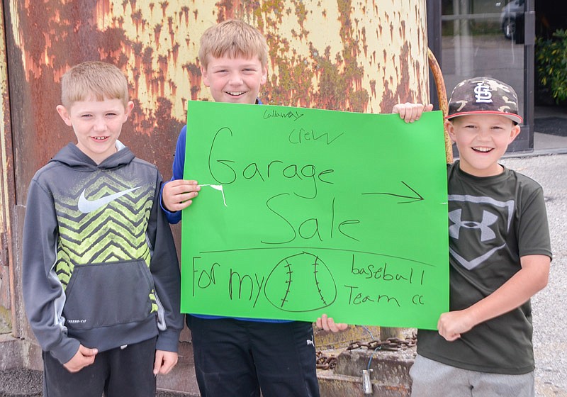 Callaway Crew players, from left, Ethan Johnson, Landon Hilderman and Caleb Sheets hold up their hand-made sign, hoping to attract customers to their garage sale Saturday morning, April 22, 2017 at 54 Country