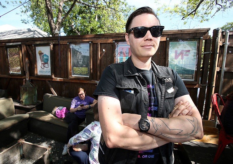 In this Friday, April 7, 2017, photo, artist Shay Scranton stands near some of his art work located on the outside walls of the local coffee shop Common Grounds, in Waco, Texas. Scranton not only creates concert posters for bands and fans but has an online store to sell pins and patches.