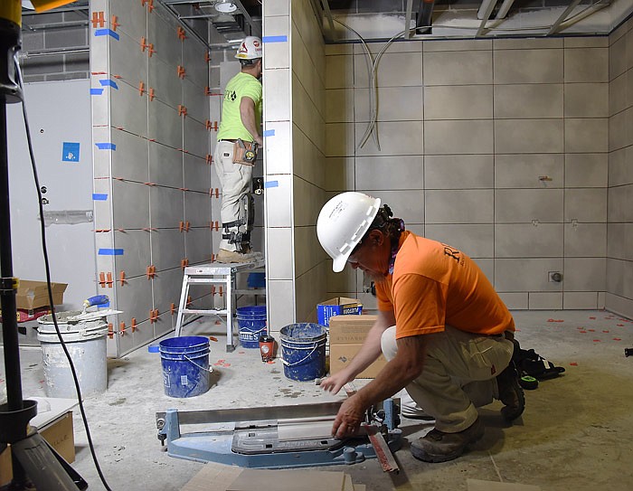 This May 2017 photo shows Jason Kellogg, on platform at left, adhering tile to the wall while Donny Carter, at right, cuts another piece for the shower wall while constructing the Lincoln University Blue Tigers football locker room at The LINC. They both work for Richardet Floor Covering in Perryville, Mo.