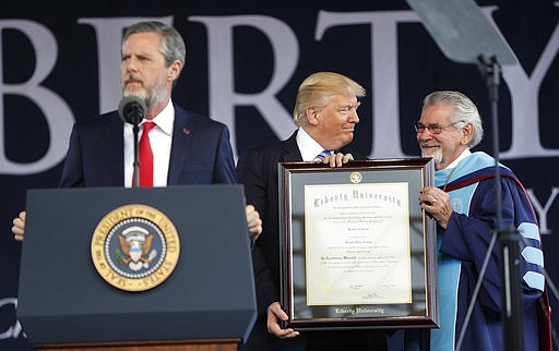 President Donald Trump, center, is presented an Honorary Degree by Ronald E. Hawkins, right, Provost and Chief Academic Officer, before giving the commencement address for the Class of 2017 at Liberty University in Lynchburg, Va., Saturday, May 13, 2017. Speaking at the podium is Liberty University President Jerry Falwell, left. 