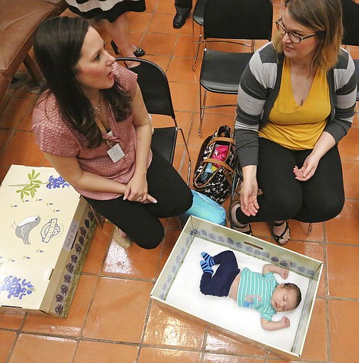 In a May 3, 2017 photo, new mothers Rachel Salinas, left, and Taylor Freed visit as six-week-old Mason Salinas relaxes in a baby box after a press conference announcing the partnering of local startup the Baby Box Company, with Dallas Medical Center at the facility in north Dallas.. The box is intended to provide a safe space for sleeping for a baby, as well as educating those who receive it about keeping children safe and alive while they are sleeping. 