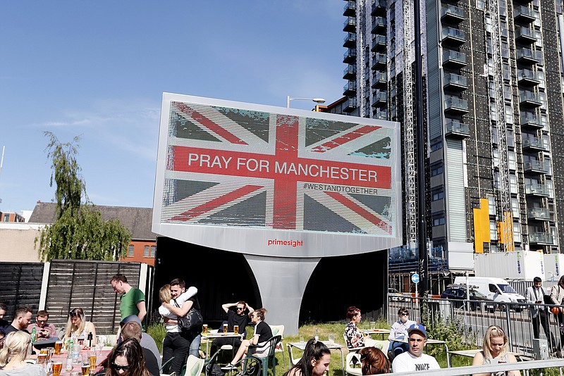 People sit under a billboard in Manchester city centre, Tuesday May 23, 2017, the day after the suicide attack at an Ariana Grande concert that left 22 people dead as it ended on Monday night.