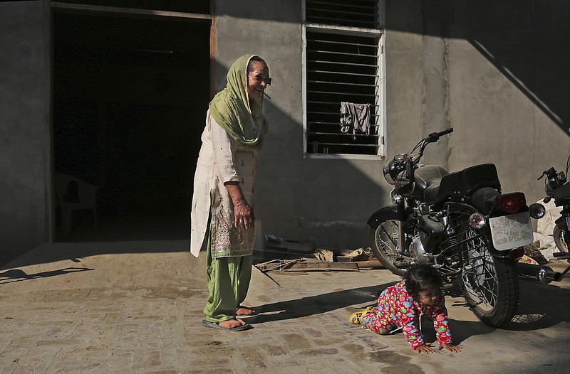 In this Dec. 23, 2016, photo, Manjeet Kaur, left, watches her daughter Gurjeet crawling in the compound of their house in Ellenabad, India. Gurjeet is the child Kaur yearned for desperately, after 40 years of being that thing which a rural Indian woman dreads more than almost anything else—barren. She gave birth at 58 years old, with help from a controversial IVF clinic in this corner of north India that specializes in fertility treatments for women over 50.