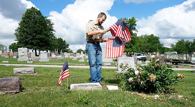 Auxvasse Boy Scout Justus Love sorts flags he was placing on soldiers' graves Wednesday at Hillcrest Cemetery in Fulton.