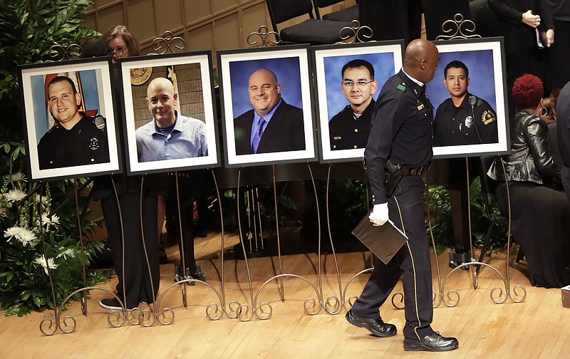 FILE - In this July 12 2016 file photo, a member of the Dallas Police Choir passes the portraits of five fallen officers prior to a memorial service at the Morton H. Meyerson Symphony Center in Dallas.  More than a dozen states this year have passed "Blue Lives Matter" laws that come down even harder on crimes against law enforcement officers. The new laws came in reaction to a spike in deadly attacks on police last year. Some civil rights activists fear the measures could set back police-community relations.