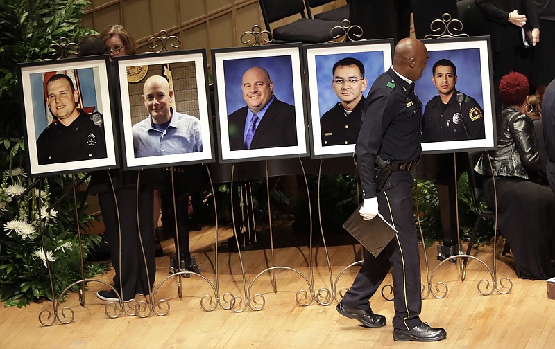 In this July 12, 2016, file photo, a member of the Dallas Police Choir passes the portraits of five fallen officers prior to a memorial service at the Morton H. Meyerson Symphony Center in Dallas. More than a dozen states this year have passed "Blue Lives Matter" laws that come down even harder on crimes against law enforcement officers. The new laws came in reaction to a spike in deadly attacks on police last year. Some civil rights activists fear the measures could set back police-community relations.
