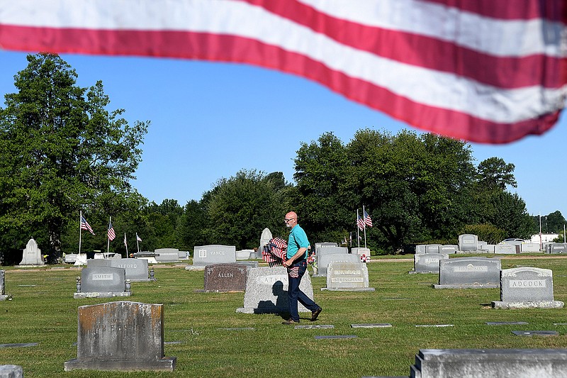 Dale Buster walks through Hillcrest Memorial Park on Thursday, placing U.S. flags at the gravestones of military veterans in preparation for Memorial Day. This marks the 25th and final year Buster will be setting up the flags.