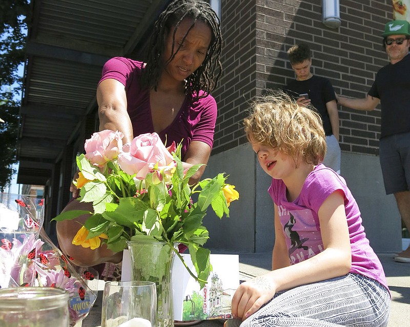 Angel Sauls, left, helps her stepdaughter, Coco Douglas arrange a sign and some painted rocks she made for a memorial in Portland, Ore., on Saturday, May 27, 2017, for two bystanders who were stabbed to death Friday while trying to stop a man who was yelling anti-Muslim slurs and acting aggressively toward two young women.