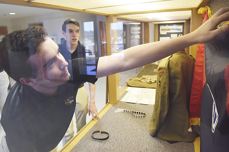 Luke Davis reaches to hang up a 129th Field Artillery Regiment banner in the display case Tuesday at the Missouri National Guard Headquarters. Davis and fellow history major, Michael Monahan, background, are interning this summer at the Museum of Missouri Military History and building a display about the 35th Infantry and its exploits in WWI.