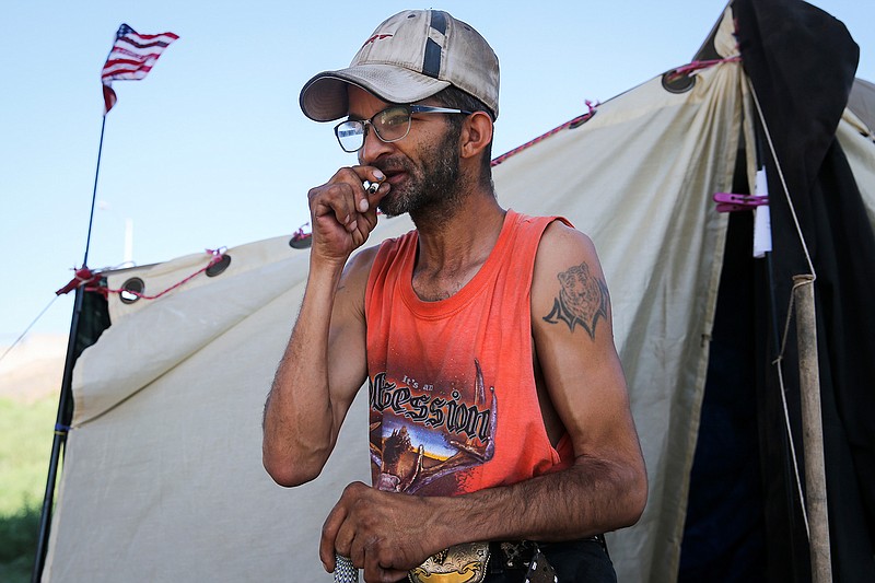 In this May 19 2017 photo, Reggie Felton lights a cigarette in tent city under the Houston Harte Expressway in San Angelo, Texas. 