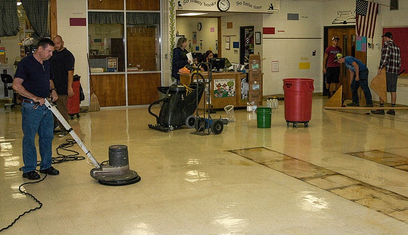 In the foreground of the photo, from left, are maintenance workers Cliff Sampson, Spencer Kimball, Rhett Kiesling, Turner Myers and Nathan Pickering. At the desk are retiring librarian Leslie Williams and the new librarian, Jill Kirksey. The rectangular marks where the shelving rested on the floor for about 40 years requires special care and extra work.