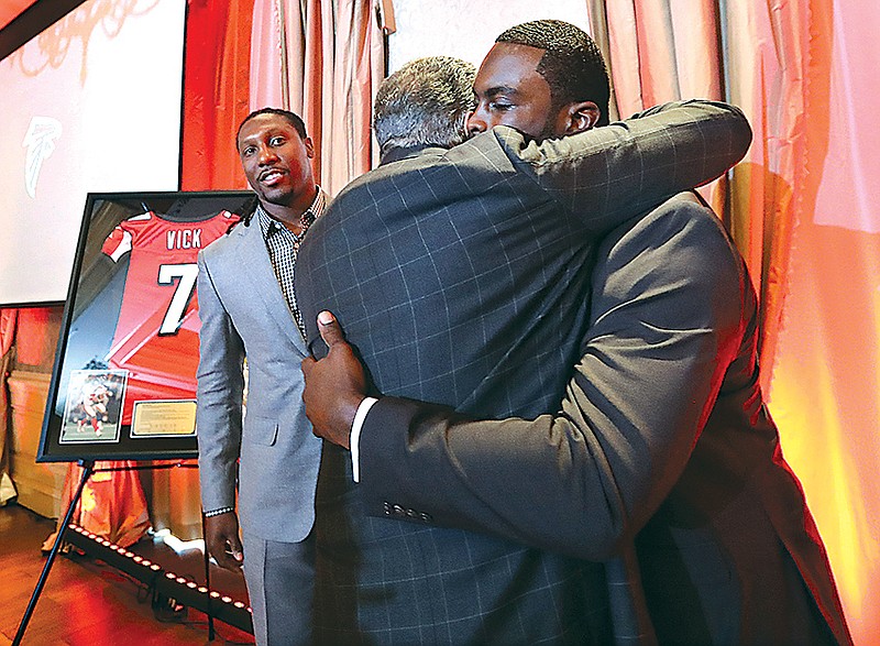 Former Atlanta Falcons quarterback Michael Vick hugs owner Arthur Blank with wide receiver Roddy White looking on as the Atlanta Falcons honor Vick and White as they officially retire from the NFL on Monday, June 12, 2017, in Atlanta.