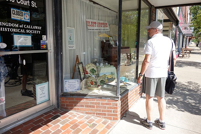 A passerby checks out auction items in the window of the Kingdom of Callaway Historical Society on Tuesday. The silent bid auction starts today and concludes at noon on July 15.