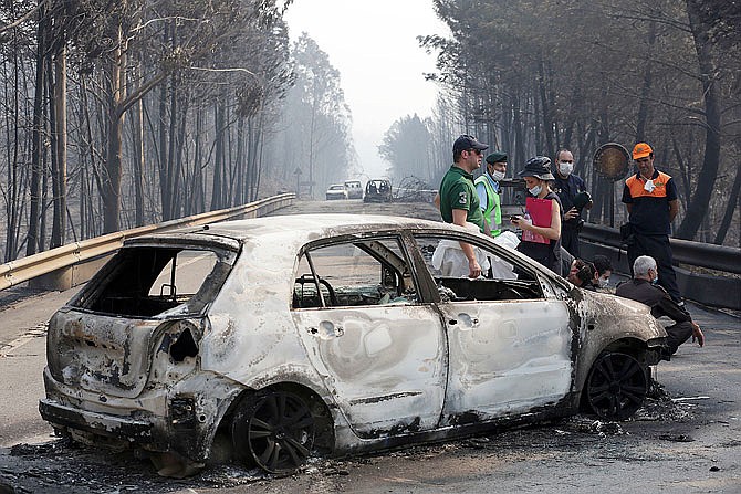 Police investigators stand by a burnt car on the road Sunday between Castanheira de Pera and Figueiro dos Vinhos, central Portugal. Raging forest fires in central Portugal killed more than 60 people, many of them trapped in their cars as flames swept over a road.