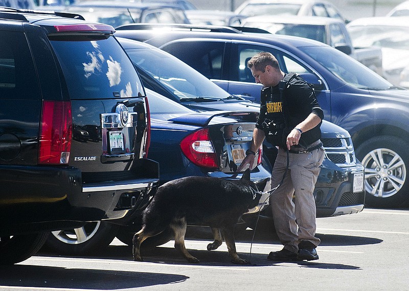 A police dog and handler search cars in a parking lot at Bishop International Airport, Wednesday morning, June 21, 2017, in Flint, Mich. Officials evacuated the airport Wednesday, where a witness said he saw an officer bleeding from his neck and a knife nearby on the ground. Authorities say the injured officer's condition is improving. (Jake May/The Flint Journal-MLive.com via AP)